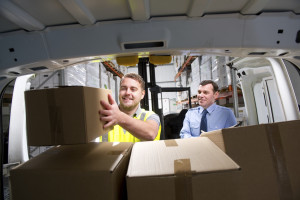 Warehouse worker loads a delivery van as his manager stands in the background.