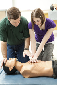 Teen girl practicing CPR on a mannequin, with her teacher's help.
